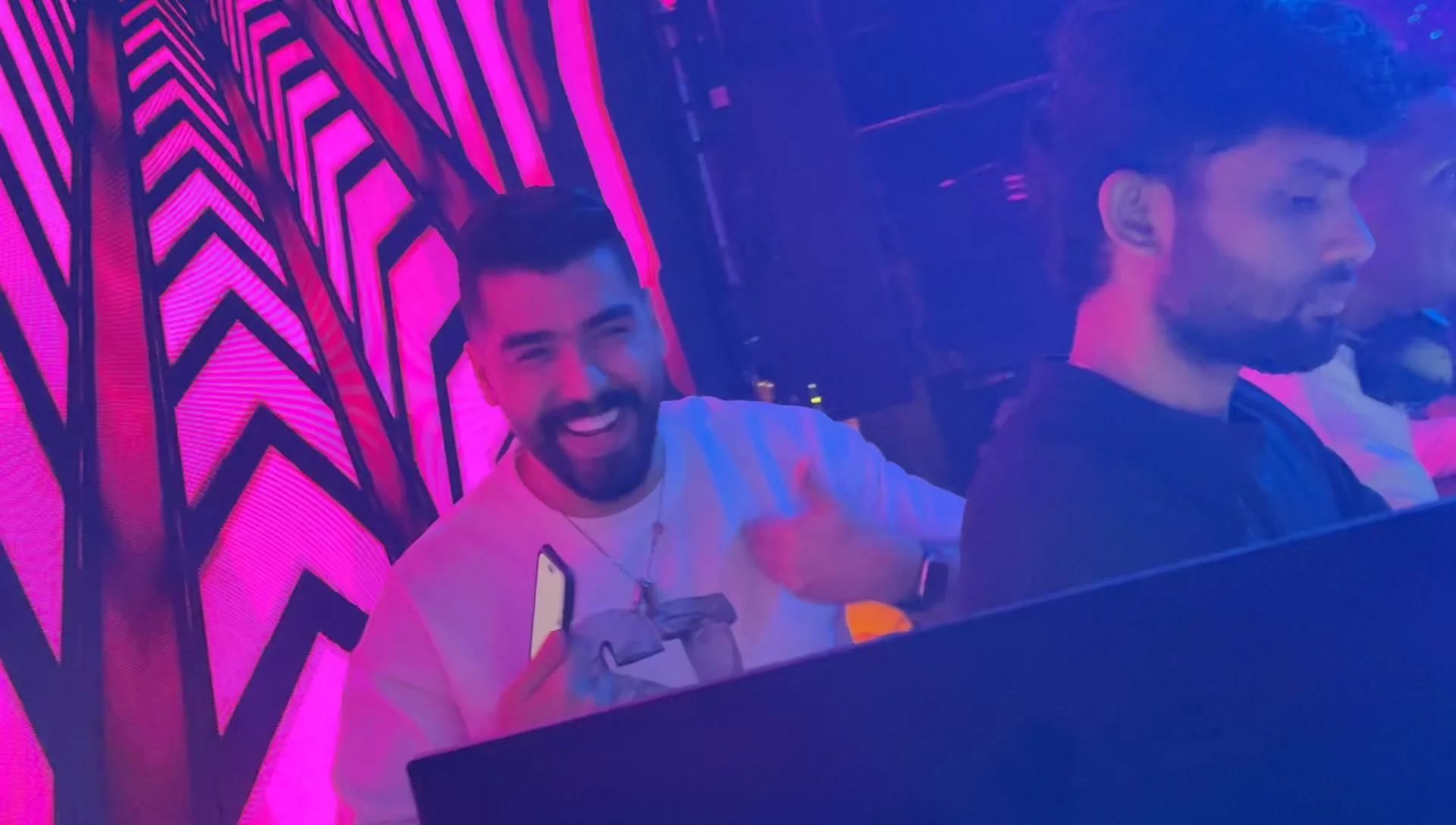 Resident DJ smiling behind the mixer decks with vivid geometric visual graphics on stage at XOXO Nightclub & Lounge Dubai